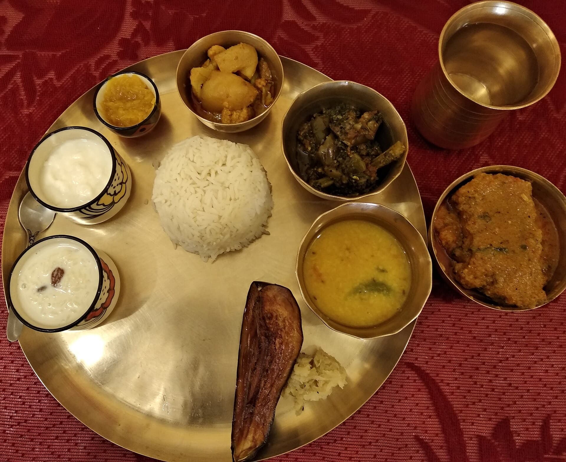 A Bengali thali on bell metal: rice in the middle, dal, fish, begun bhaja and doi in bowls around it