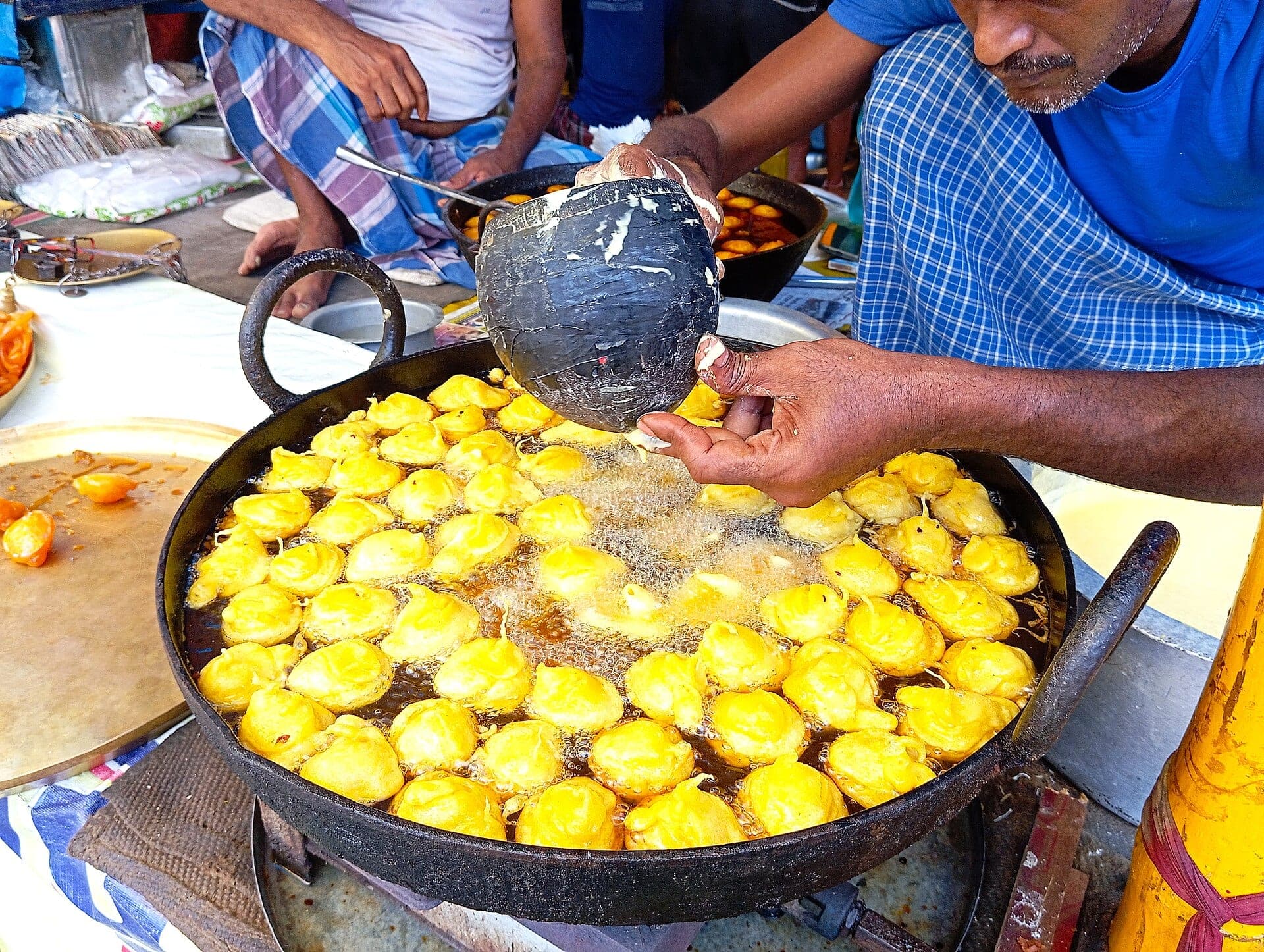 A street vendor frying sweets in a wide karai