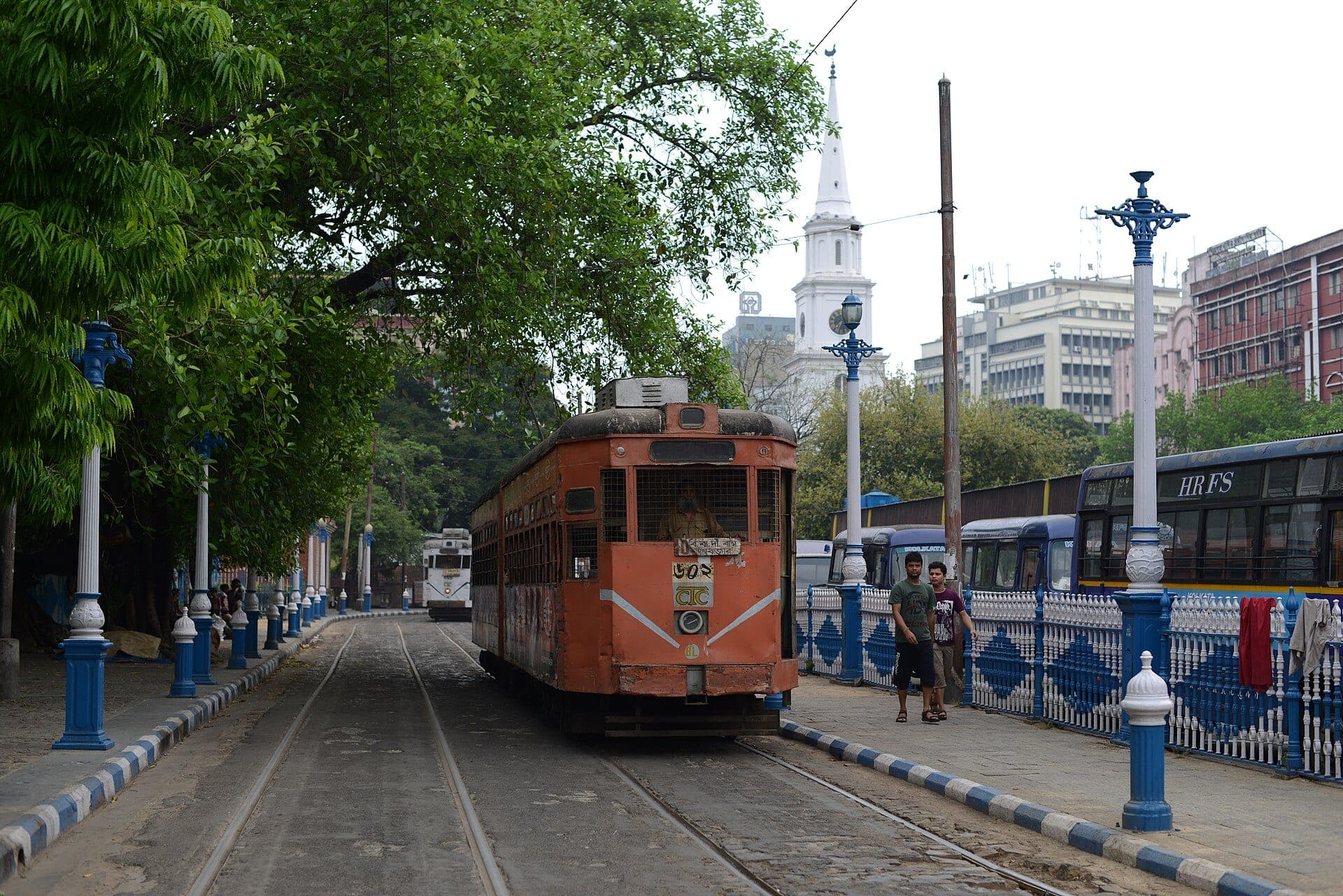 An orange Kolkata tram on a tree-lined street